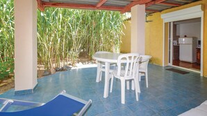 A covered patio with a table and chairs, a blue lounge chair, and a kitchen visible through an open doorway. - 1 bedroom beautiful home in Calvi (Calvi)