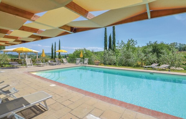 A swimming pool with lounge chairs and umbrellas, surrounded by greenery and tall trees.