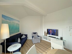Una sala moderna con un sofá azul oscuro, un sillón a rayas, una mesa blanca y un televisor montado en la pared.
