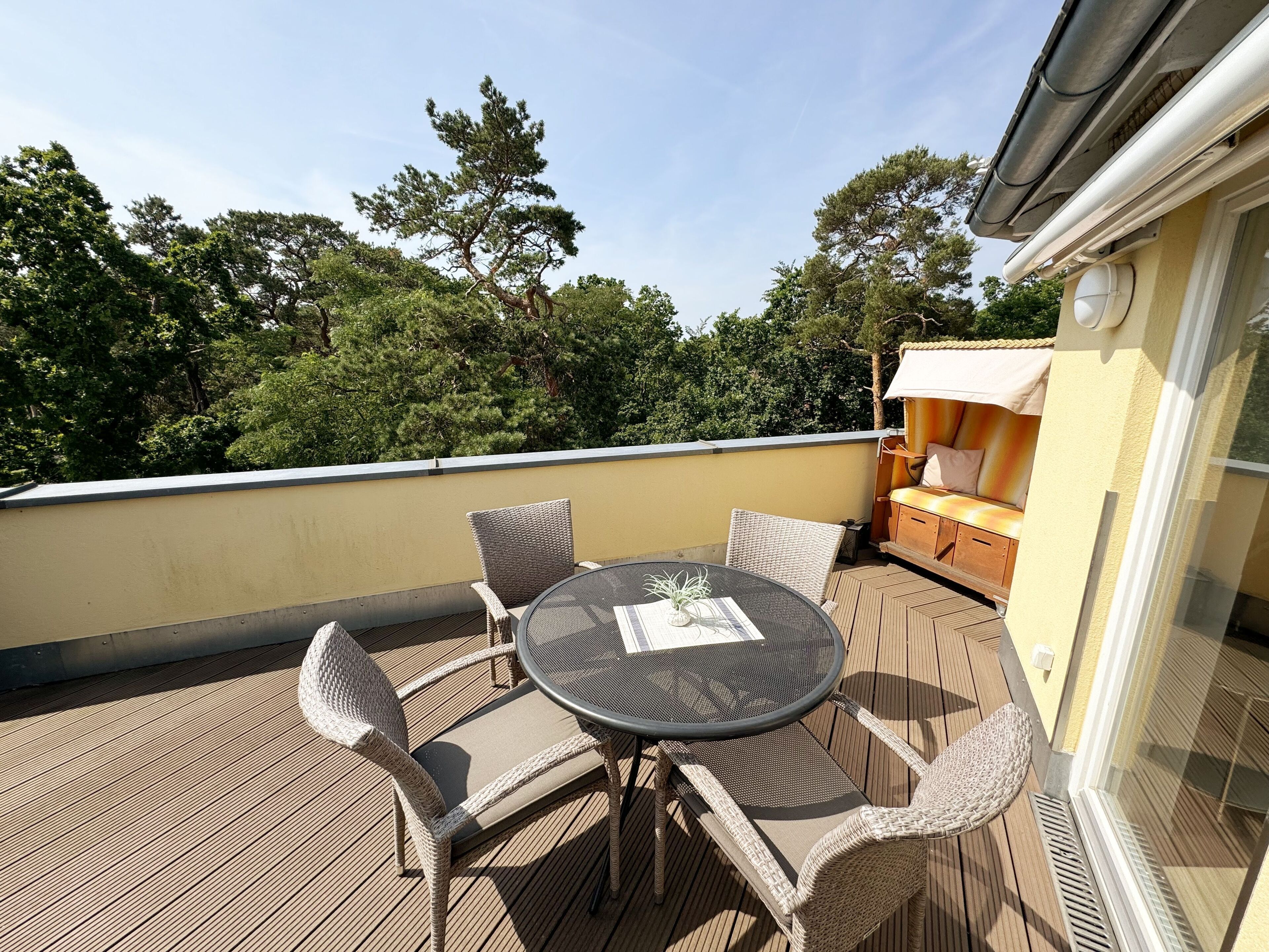 Um deck de madeira com uma mesa redonda e cadeiras de vime, com vista para uma paisagem verde exuberante.