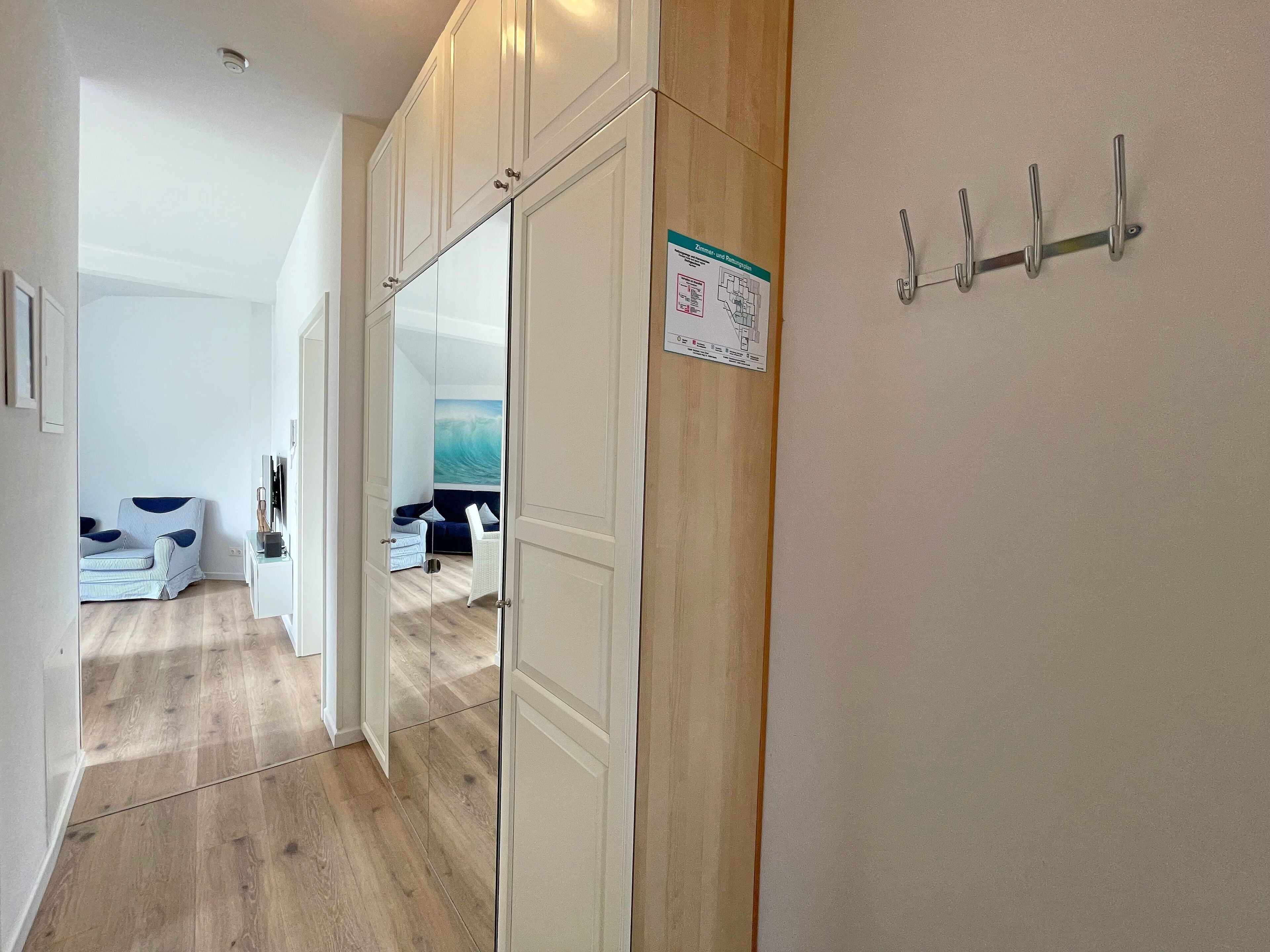 Un pasillo con puerta de armario espejada, piso de madera, pared blanca con un mapa y perchero de pared.