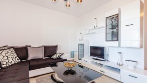 Ett modernt vardagsrum med en mörkbrun soffa, ett soffbord i glas, en platt-TV och en vit TV-möbel med hyllor i glas.