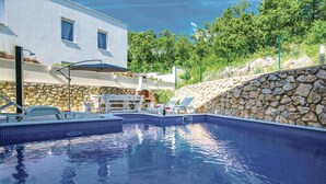 En swimmingpool med solstolar, en stenmur och en byggnad med fönster.