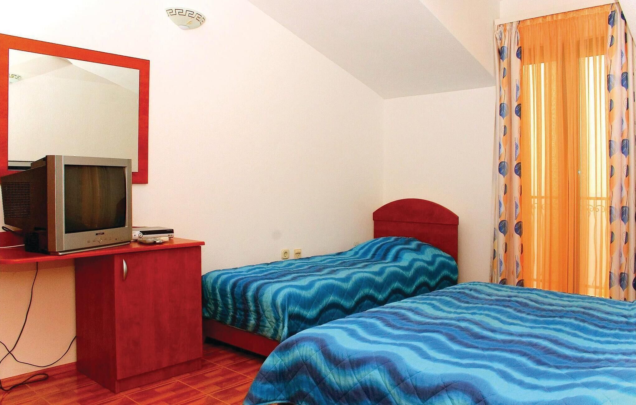 A small room with two beds, a TV on a desk, and a mirror.