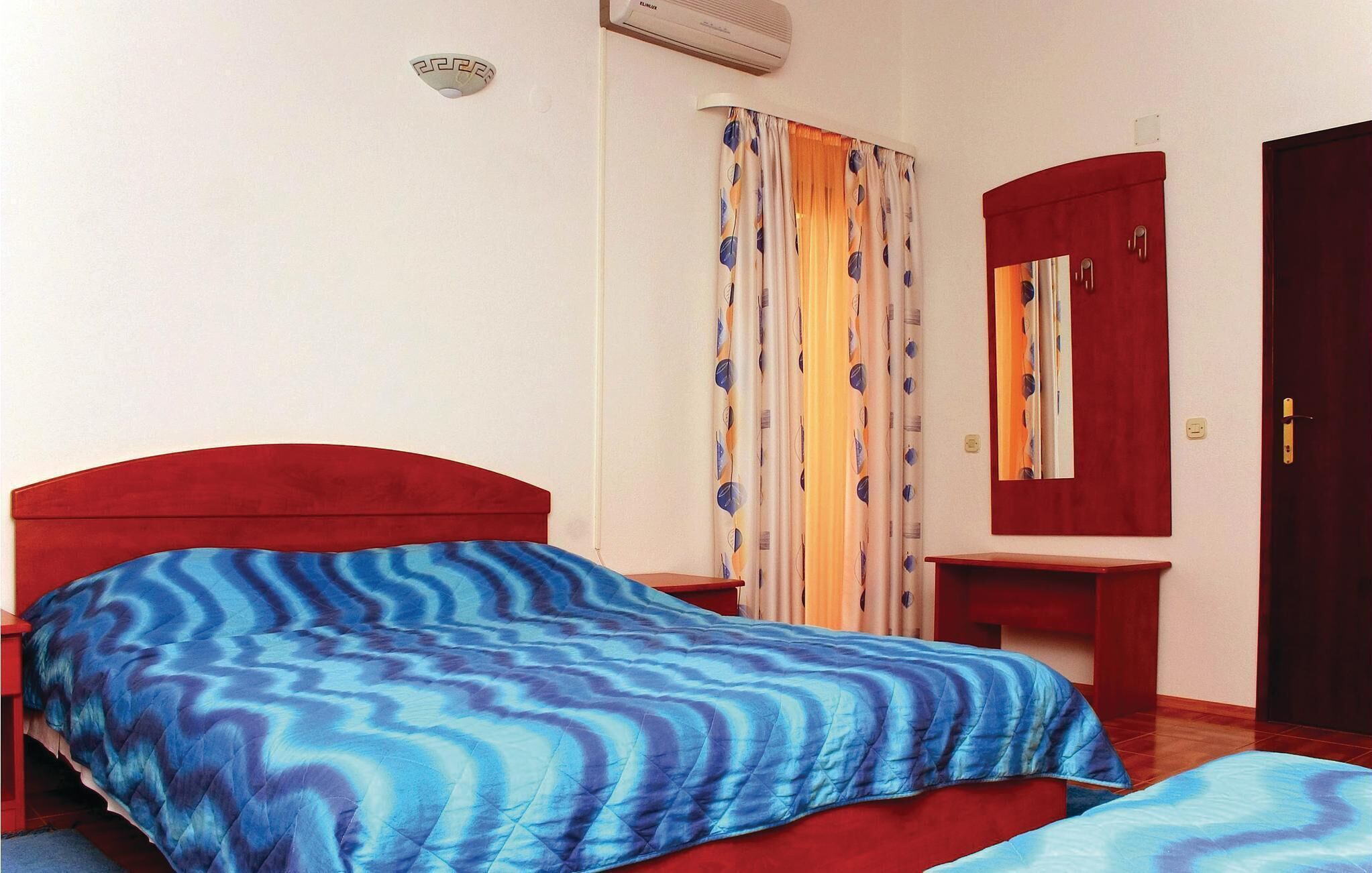 A room with a bed, a bedside table, a mirror, and a wardrobe.