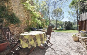 An outdoor patio with a round table covered by a yellow tablecloth, two wooden chairs, and a stone wall. - 1 bedroom amazing apartment in Lorgues (Lorgues)
