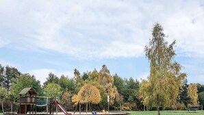 Un parque infantil con tobogán, columpios y estructura para escalar, en un parque con árboles y césped.