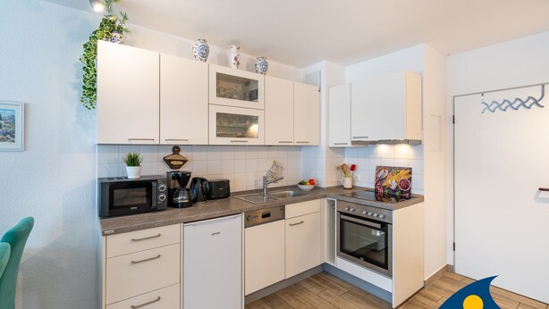 Una cocina moderna con armarios blancos, horno empotrado, microondas y cafetera.