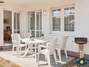 Un patio con una mesa redonda y sillas blancas, una parrilla y una planta en maceta.