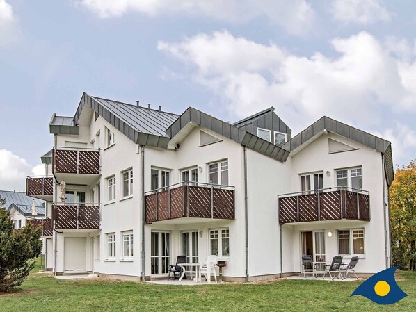 A modern multi-story residential building with balconies, a covered outdoor seating area, and a well-maintained lawn.