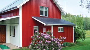 A red two-story house with a sloped roof, a front porch, and a small garden with pink flowers. - 2 bedroom nice home in Töcksfors (Töcksfors)