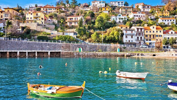 A coastal village with houses on a hillside, a stone pier, and boats in the water.