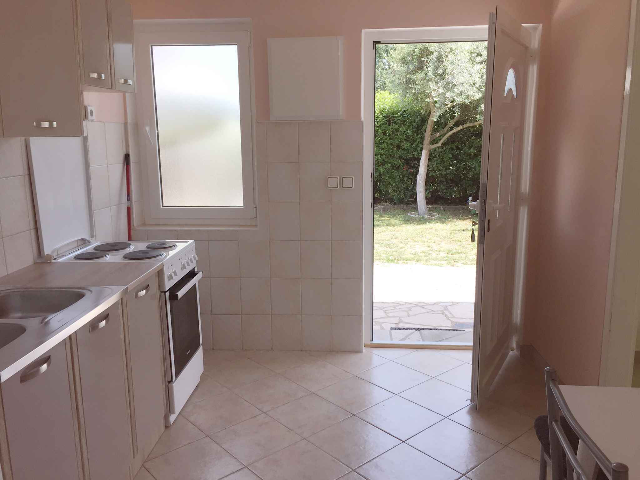 A kitchen with a gas stove, oven, and sink. There is a window and a door leading outside.