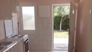 A kitchen with a gas stove, oven, and sink. There is a window and a door leading outside.