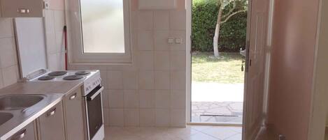 A kitchen with a gas stove, oven, and sink. There is a window and a door leading outside.