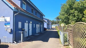 Een blauw gebouw met genummerde deuren, een verhard pad en een hek met een verkeersbord voor de maximumsnelheid.