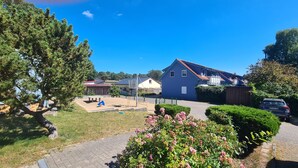 Een woonwijk met een blauw huis, een speeltuin en een geparkeerde auto in de buurt.