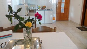 Een keuken met witte kastjes, een spoelbak en een houten deur. Op de tafel staat een vaas met bloemen.