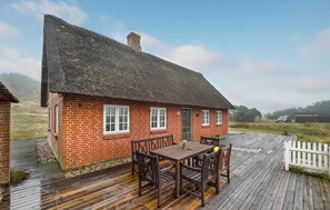 Ein Backsteinhaus mit einem Strohdach und einer Holzterrasse.