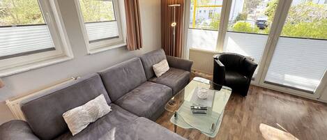 A modern living room with a grey sectional sofa, a glass coffee table, and a black armchair.