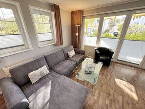 Moderni olohuone, jossa on harmaa kulmasohva, lasinen sohvapöytä ja musta nojatuoli.