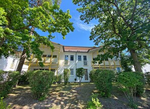 A two-story building with a yellow balcony, surrounded by trees and greenery.