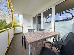 A patio with a wooden table and chairs, a glass door leading to a covered area, and a view of the neighborhood.