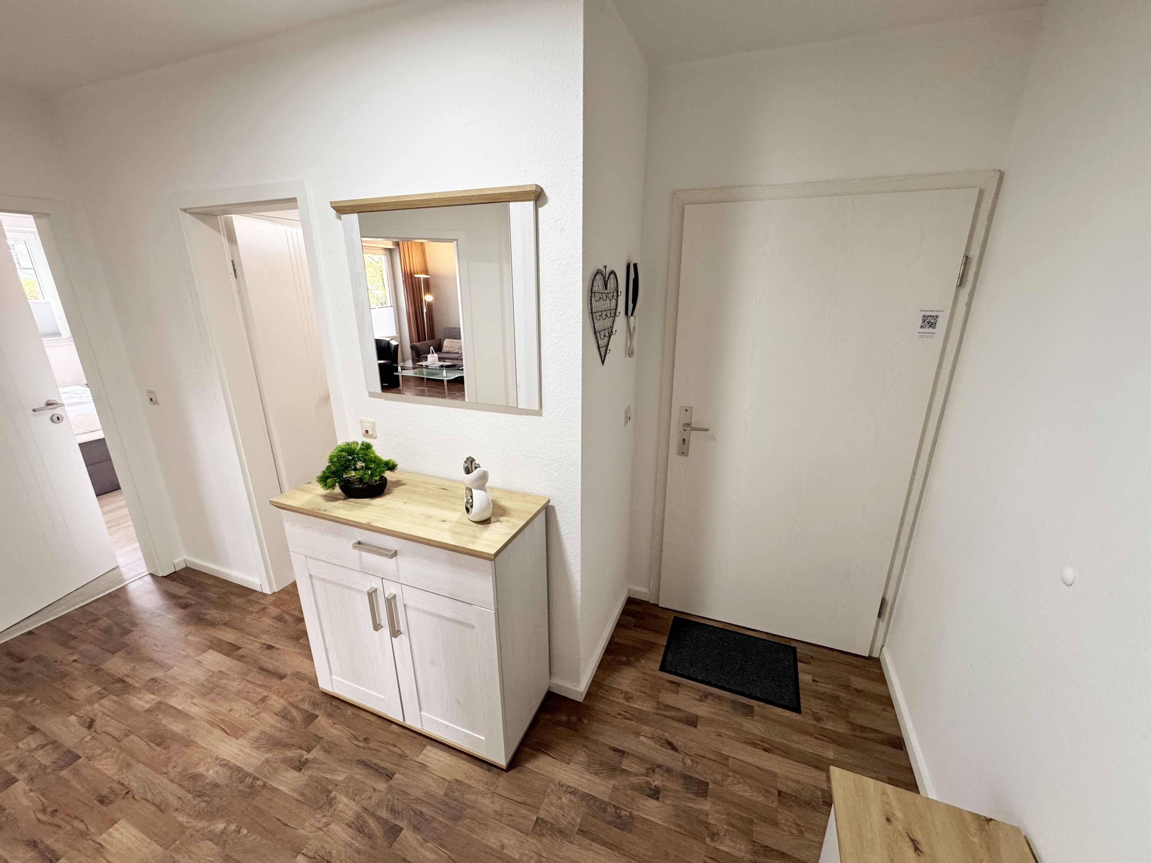 Een moderne badkamer met een houten wastafel, een spiegel, een plant in pot en een deur naar een andere kamer.