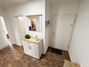 Ein modernes Badezimmer mit Waschtisch aus Holz, einem Spiegel, einer Topfpflanze und einer Tür zu einem weiteren Raum.
