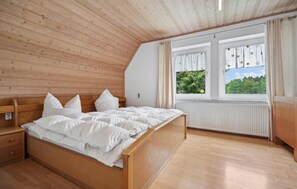 Een slaapkamer met een houten plafond, een bed met wit beddengoed, een nachtkastje en een raam met gordijnen.