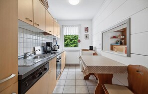Een kleine keuken met een spoelbak, fornuis en een eethoek met een tafel en stoelen.