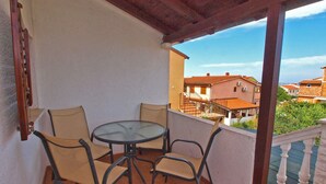 A balcony with a table and four chairs, overlooking a residential area with houses and a clear sky. - Holiday apartment mit Terrasse und Klimaanlage (Peroj)