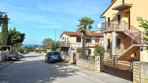 A residential street with stone walls, a blue car parked on the side, and a clear view of the sea in the background. - Holiday apartment mit Terrasse und Klimaanlage (Peroj)