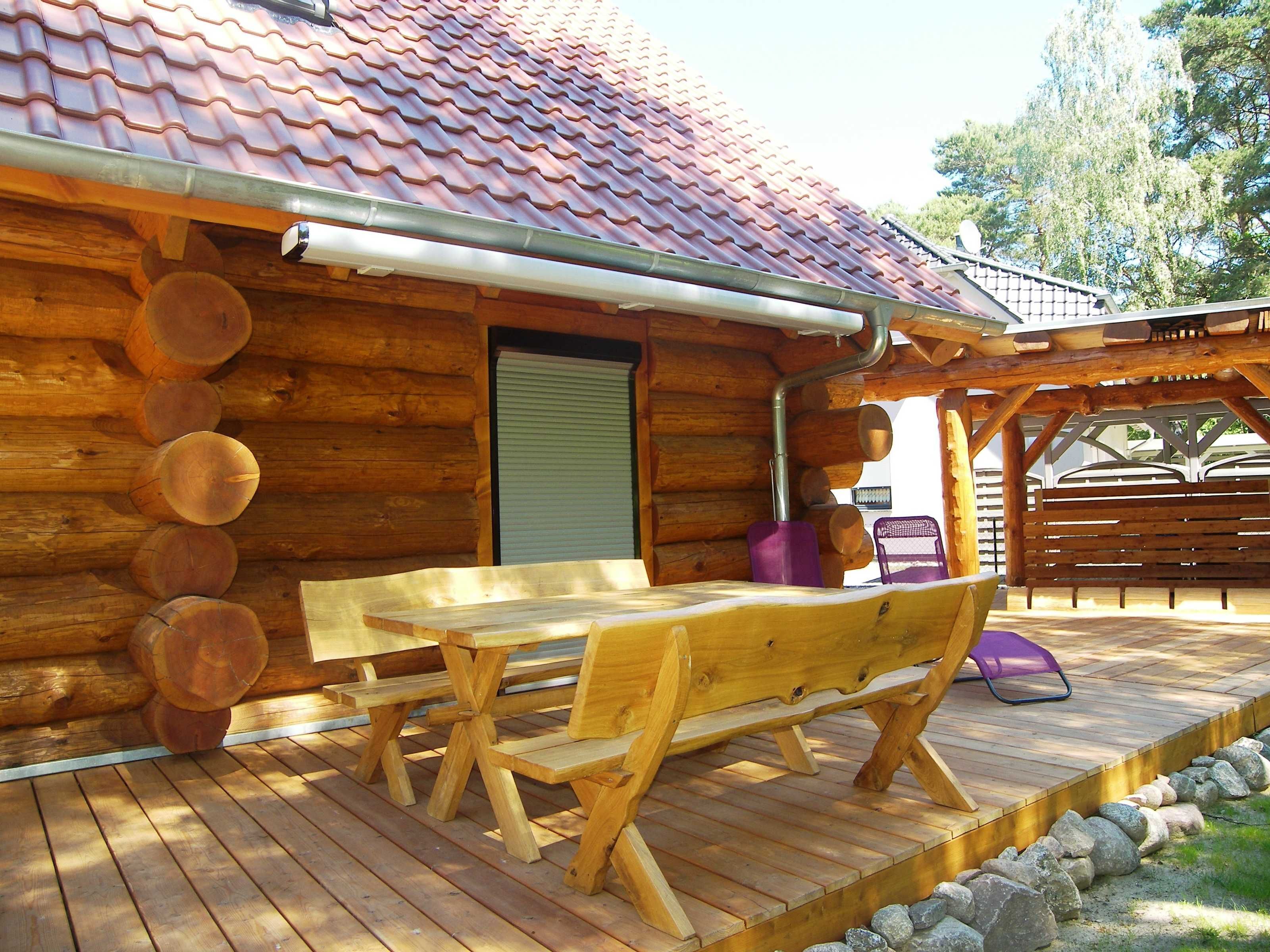 Una cabaña de madera con techo de tejas, una terraza de madera con bancos y un porche cubierto.