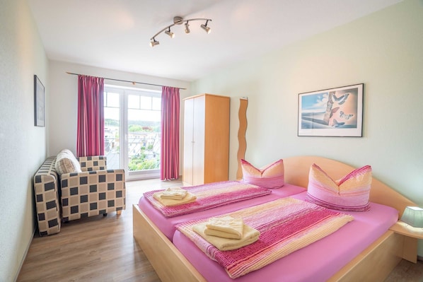 Une chambre à coucher avec un lit, deux chaises, une armoire et une fenêtre avec des rideaux.