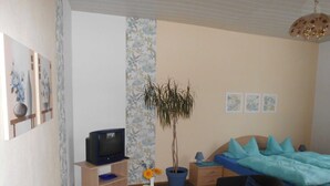 Une chambre à coucher avec un lit, une télévision, une petite table avec un vase et une plante en pot.