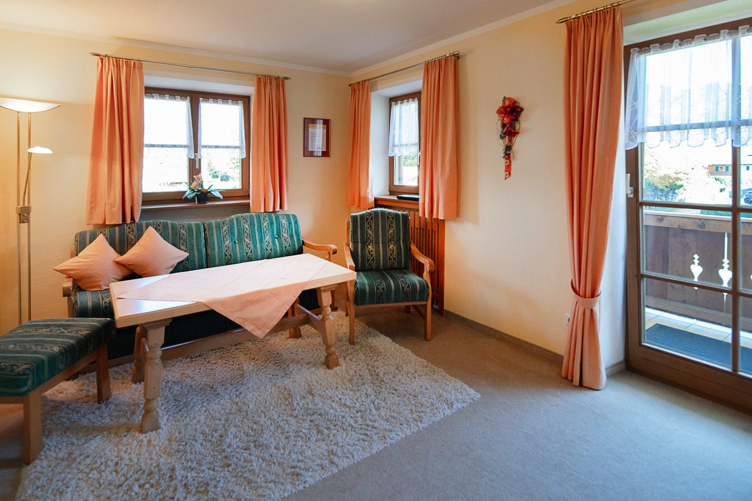 A room with a sofa, a table, and two chairs, a window with curtains, and a lamp.