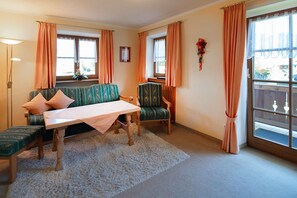 A room with a sofa, a table, and two chairs, a window with curtains, and a lamp. - Apartment 2 - Vacation Lohbinder (Fam. Holzer) (Rottach-Egern)
