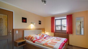A bedroom with a wooden bed, a nightstand, a window with curtains, and a mirror on the wall. - Apartment 2 - Vacation Lohbinder (Fam. Holzer) (Rottach-Egern)