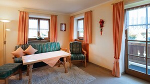 A room with a sofa, a table, and two chairs, a window with curtains, and a lamp. - Apartment 2 - Vacation Lohbinder (Fam. Holzer) (Rottach-Egern)