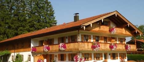 A two-story building with balconies, a wooden facade, and flower arrangements.