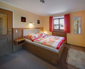 Une chambre à coucher avec un lit en bois, une table de chevet, une fenêtre avec des rideaux et un miroir au mur.