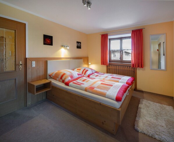 Ein Schlafzimmer mit einem hölzernen Bett, einem Nachttisch, einem Fenster mit Vorhängen und einem Spiegel an der Wand.