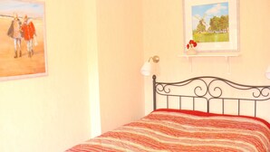 Un dormitorio con una cama, una lámpara de pared y dos cuadros enmarcados.