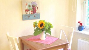 Un comedor con una mesa, sillas, un jarrón con flores, una lámpara colgante y un cuadro en la pared.