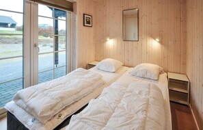 A double bed with white bedding in a room with wooden panel walls, a window, and a mirror on the wall. - Beautiful home in Ebeltoft with sauna (Ebeltoft)