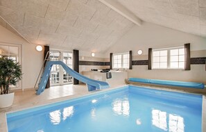 En inomhuspool med en blå vattenrutschkana, ett köksområde och en sittgrupp vid poolen.
