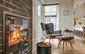 Ett mysigt vardagsrum med en öppen spis, en bekväm fåtölj och en matplats med stolar och ett bord.