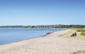 A beach with a sandy shore, a few boats on the water, and a distant town. - Beautiful home in Ebeltoft with sauna (Ebeltoft)