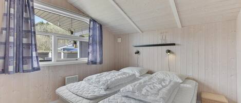 Une chambre avec deux lits, une fenêtre avec des rideaux, une plante suspendue et un petit banc.
